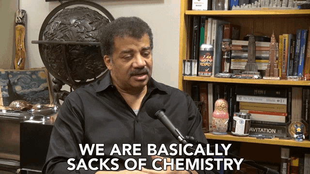 a man talking into a microphone with the words we are basically sacks of chemistry