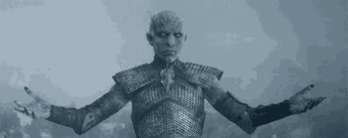 the night king from game of thrones is standing in the snow with his arms outstretched and looking at the camera .