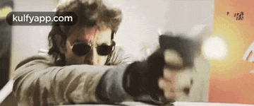 a man wearing sunglasses is pointing a gun at a target .