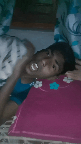 a young man laying on a bed with a pink pillow with a flower on it