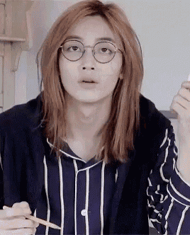 a young man with long red hair and glasses is holding a pencil and a cell phone .
