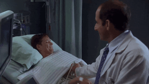 a doctor shakes hands with a patient who is laying in a hospital bed