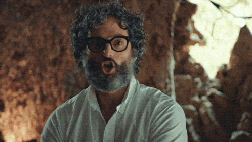 a man with curly hair and glasses is making a surprised face