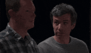 a man in a plaid shirt is talking to another man in a gray sweater