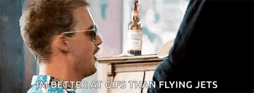 a man wearing sunglasses is talking to another man in front of a table with a bottle of beer on it .