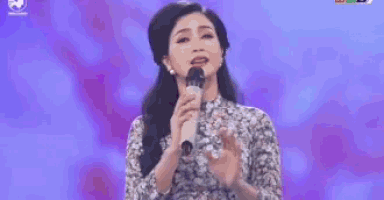 a woman is singing into a microphone on a stage with purple lights .