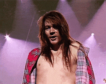 a shirtless man with long hair stands in front of a purple background