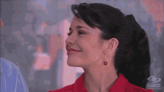 a woman wearing red earrings is smiling in front of a caracol television logo