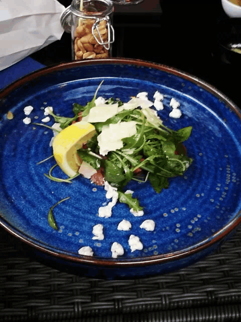 a blue plate with a salad on it and a jar of nuts in the background