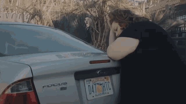 a woman leans on a silver ford focus with a florida license plate
