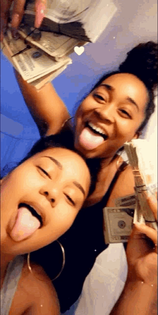 two women sticking their tongues out while holding stacks of money .