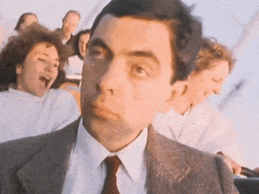 a man in a suit and tie is riding a roller coaster with a group of people .