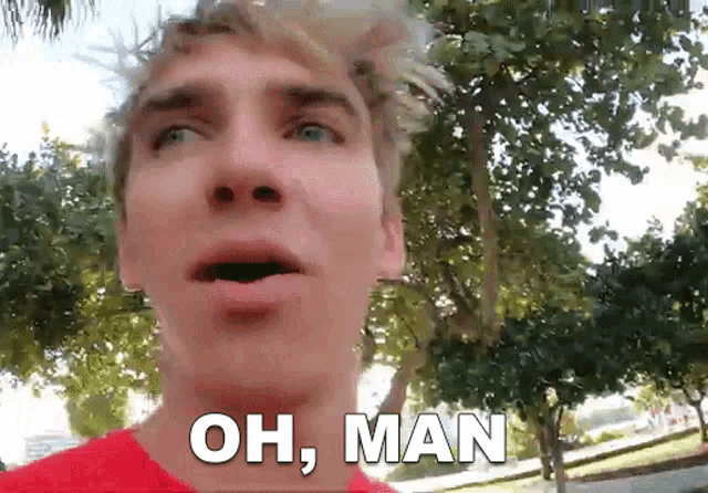 a man in a red shirt says oh man in front of some trees