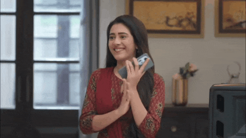 a woman is smiling while holding a cell phone in her hand .