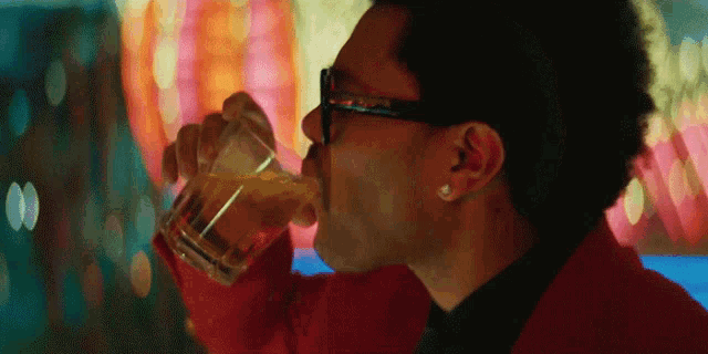 a man wearing glasses is drinking a glass of whiskey