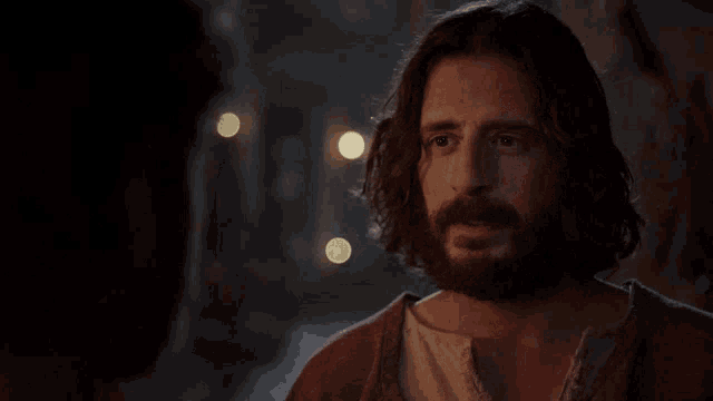 a man with long hair and a beard stands in the dark