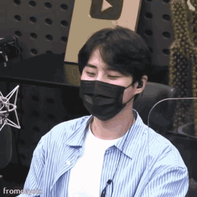 a man wearing a mask and a striped shirt is sitting in front of a microphone ..