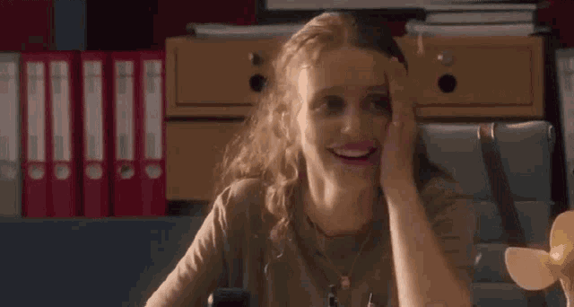 a woman is smiling with her hand on her face while sitting at a desk .