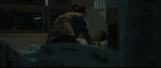 a man in a hospital gown is laying in a hospital bed talking to a woman .
