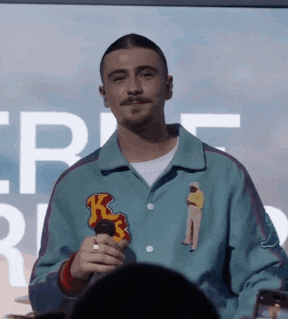 a man in a blue jacket holds a microphone with the letter k on the front