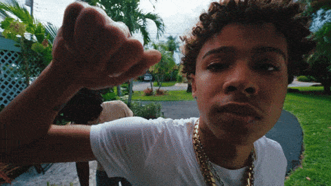 a young man wearing a white t-shirt and gold chains is making a fist