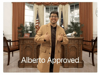a man in a tan coat is giving a thumbs up in front of a desk that says alberto approved on it