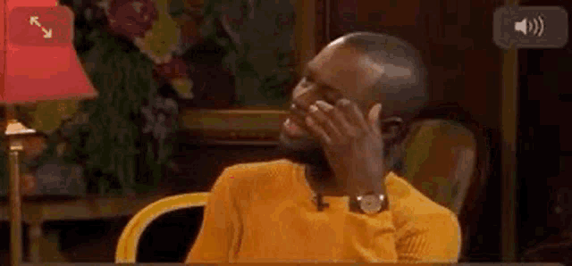 a man in a yellow sweater is sitting at a table covering his mouth with his hand .