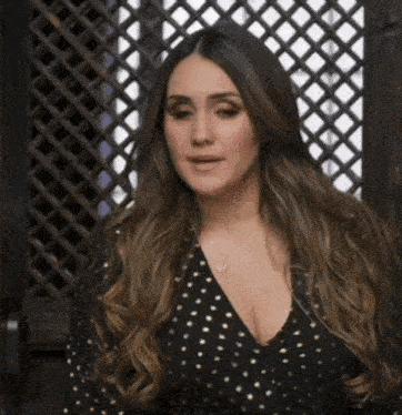 a woman wearing a black dress with gold polka dots stands in front of a wooden fence