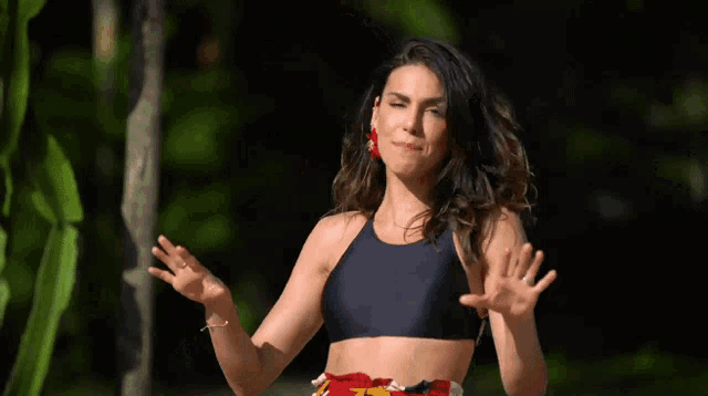 a woman in a black crop top and red earrings stands with her arms outstretched