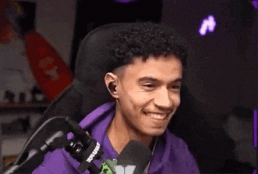 a young man in a purple hoodie is laughing in front of a microphone while sitting in a chair .