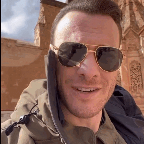 a man wearing sunglasses and a hooded jacket smiles for the camera