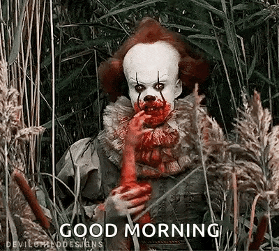 a clown with blood on his face is standing in a field of tall grass and holding a bloody hand .