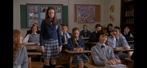 a girl in a plaid skirt stands in front of a classroom full of people