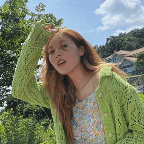 a woman with red hair is wearing a green cardigan and a floral tank top .