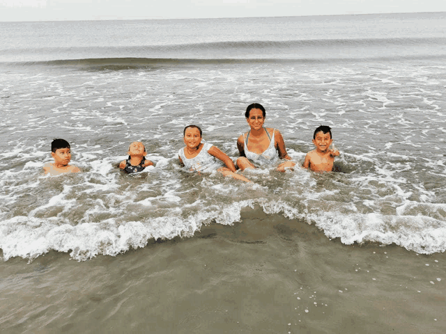 a woman and three children are sitting in the water on a beach
