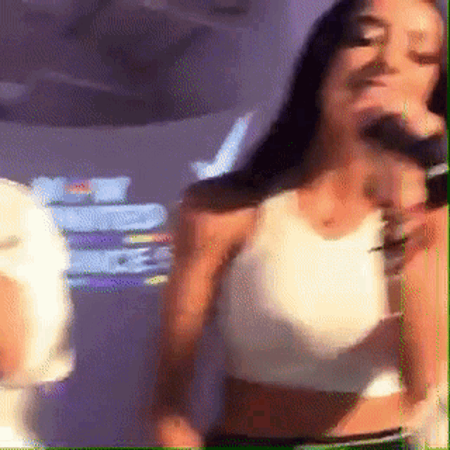 a woman in a white tank top is dancing in front of a purple wall .
