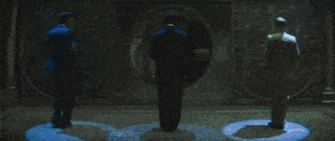 three men in suits are standing in front of a round window in a dark room .