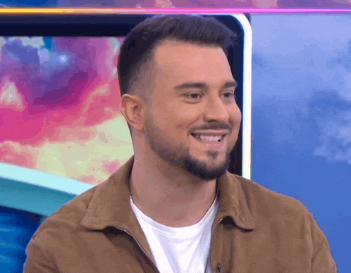 a man with a beard is smiling and wearing a brown jacket .