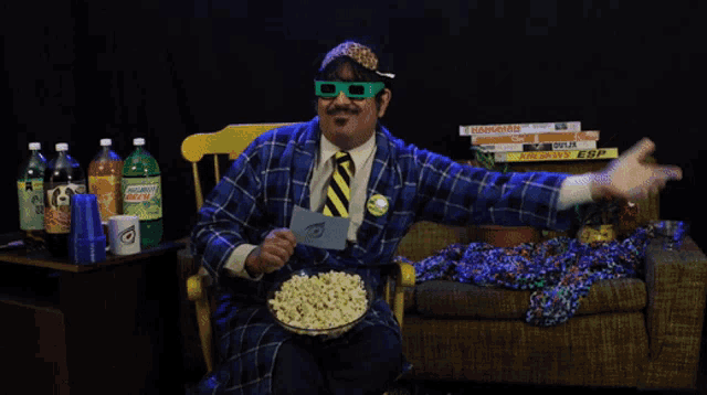 a man wearing 3d glasses is sitting on a couch eating popcorn and drinking mountain dew