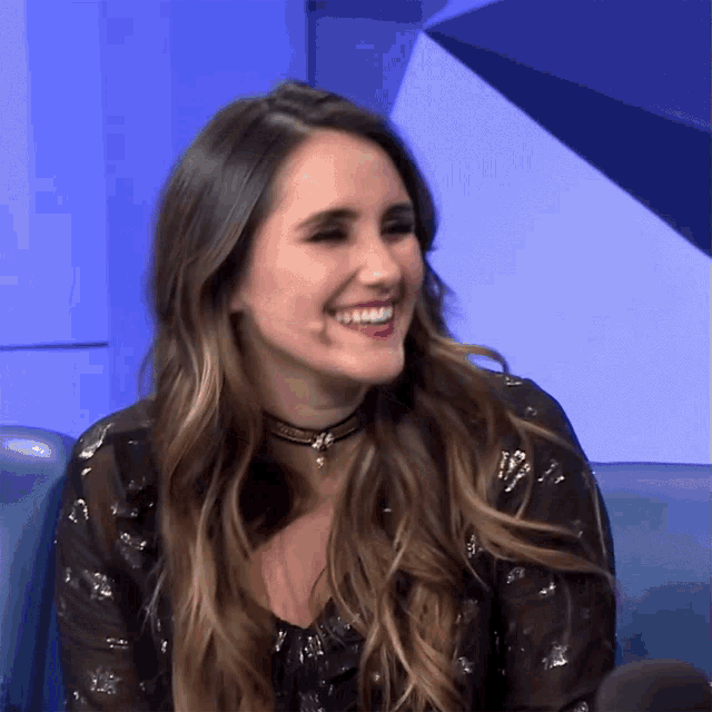 a woman wearing a choker smiles while sitting in a chair