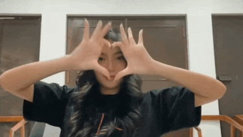 a woman is making a heart with her hands in front of her face .