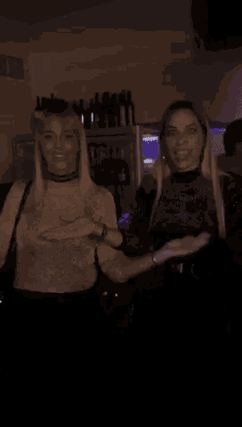 two women are standing next to each other in a dark room and smiling