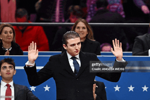 a man in a suit and tie waves his hand in front of a sign that says credit angela weiss