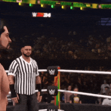 a man in a striped shirt is standing in a wrestling ring in front of a crowd