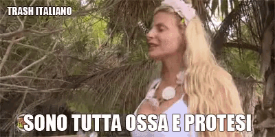 a woman in a white dress is standing in the woods with the words sono tutta ossa e protesi above her .