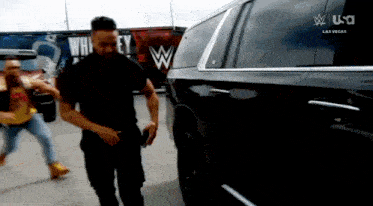 a man in a black shirt is standing in front of a black suv with a wwe logo on the side .