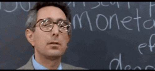 a man wearing glasses stands in front of a blackboard that says moneta