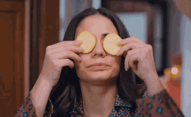 a woman covering her eyes with slices of potato