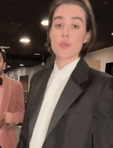 a woman in a tuxedo stands next to a man in a pink suit