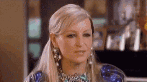 a close up of a woman wearing a necklace and earrings making a funny face .